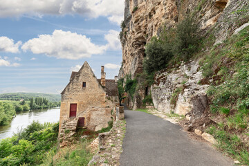 Fototapeta na wymiar Secluded stone house on road along steep cliff on one side and full-flowing bed of Dordogne river. Dordogne department, New Aquitaine region, France