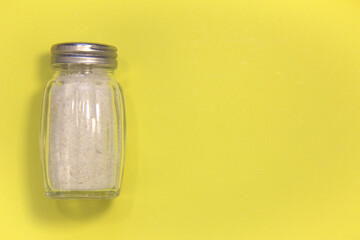 Salt in a salt shaker. On a yellow background. Close up. Place for text.