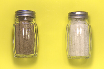 Salt and pepper in salt shakers. On a yellow background.
