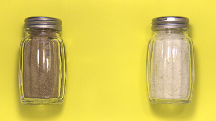 Salt and pepper in salt shakers. separately. On a yellow background. Close up.