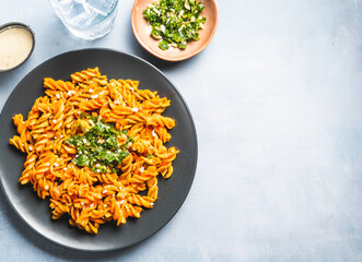 Curly pasta macaroni with tomato and gremolata sauce in a round dark plate on a table with a glass of water. Ready to eat.