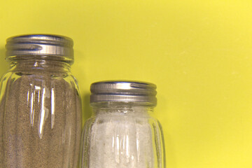 Salt and pepper in salt shakers. On a yellow background. Place for text.