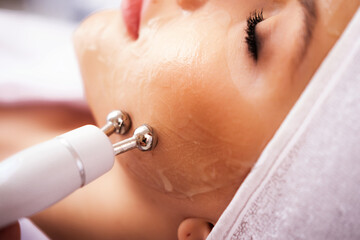 Close-up portrait of a beautiful woman with closed eyes and apparatus for skin rejuvenation. Beauty...