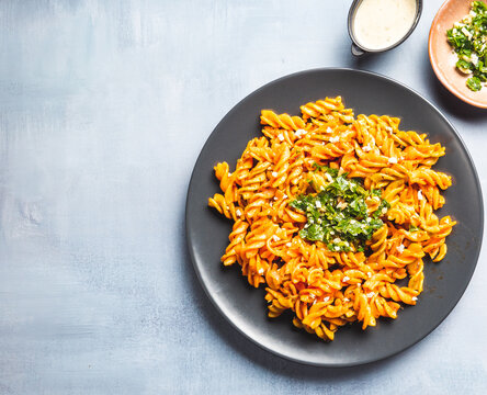Curly pasta macaroni with tomato and gremolata sauce in a round dark plate on a table. Ready to eat.