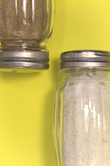 Salt and pepper in salt shakers. On a yellow background. Place for text. Vertical.