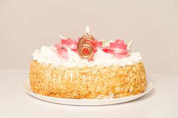 Beautiful birthday cake with the number candle 6 on a light beige background.