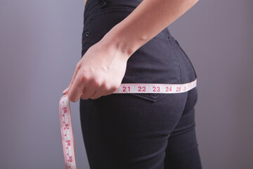 A woman measures her butt with a measuring tape.