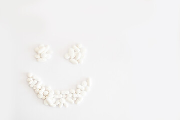 Białe lekarstwa i witaminy w tabletkach rozsypane na jasnym tle tworzą uśmiech, suplementacja diety, leczenie przewlekłe, farmacja, - obrazy, fototapety, plakaty