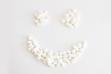 Białe lekarstwa i witaminy w tabletkach rozsypane na jasnym tle tworzą uśmiech, suplementacja...