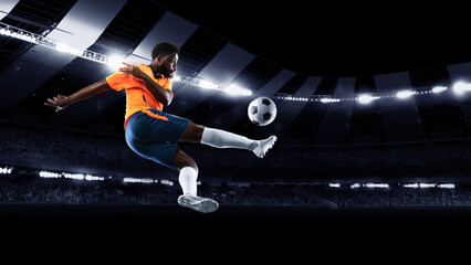 Young professional football or soccer player in motion on stadium with flashlights, kicking ball...