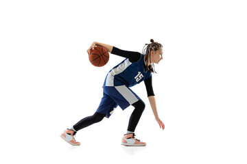 Full-length side view studio shot of young girl, basketball player in blue uniform training isolated over white background. Dribbling