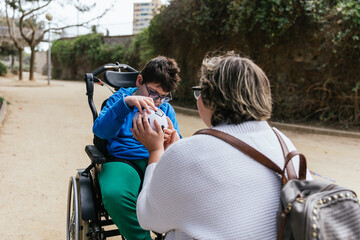 Boy with multiple disabilities playing with a soccer ball with his mother outdoors in the park.