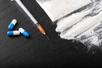 Cocaine or other illegal drugs, white powder, money, pills, syringe on black background.