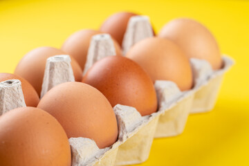 Chicken brown fresh raw eggs in an egg container n a yellow background. Ingredients for cooking. Healthy eating is a concept.