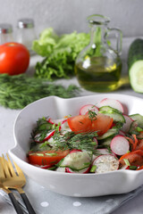 Salad with cucumbers, tomatoes and radishes dressed with olive oil in white salad bowl on a gray background