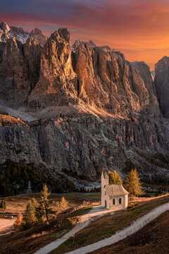 South Tyrol, Italy - The Chapel of San Maurizio (Cappella Di San Maurizio) at the Passo Gardena Pass in the Italian Dolomites at autumn with warm colorful sunset sky and clouds