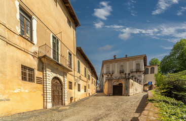 Fototapeta na wymiar Saluzzo, Cuneo, Italy - April 15, 2022: Via Pusterla, cobbled street in the ancient city with historic ancient buildings on blue sky with clouds