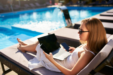 Woman doing remote multitasking work with multiple electronic internet devices on swimming pool...