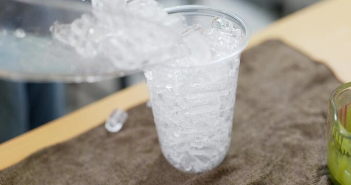 Pouring ice cube into a plastic glass.