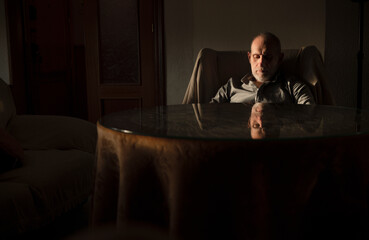 Fototapeta premium Adult man sitting on sofa chair in living room with sunlight and shadow