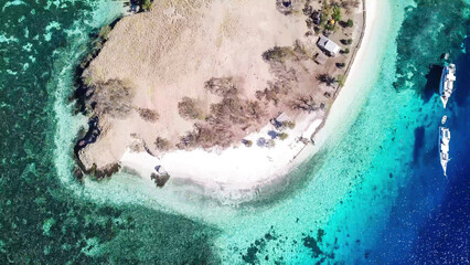 Top down drone shot of paradise island in Komodo National Park, Flores, Indonesia. The island has scarcely any plants and is surrounded with idyllic white sand beaches. Few boats anchored on the shore