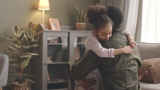Slowmo of young African American army officer in military uniform returning home after long assignment, embracing his 6 year old daughter with tenderness