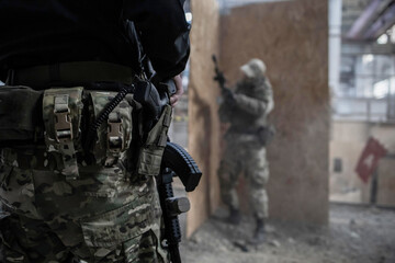 A selective focus shot of a police officeror soldier holding a rifle in front of a blurry background with a man reloading a automatic rifle.