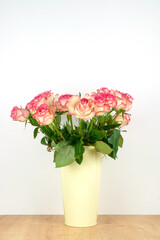 Close-up of a lot of pink and white roses in a tin vase with handles on a wooden table on a neutral background. Vertical photo