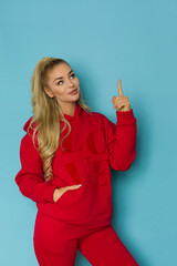 Happy woman in red sweatpants and hooded sweatshirt is pointing up. - 500404715