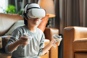 exiting asian child male boy enjoy metaverse gaming with wearable vr headset with control handle playing sport gaming online in living room at home,home technology young teen using vr technology