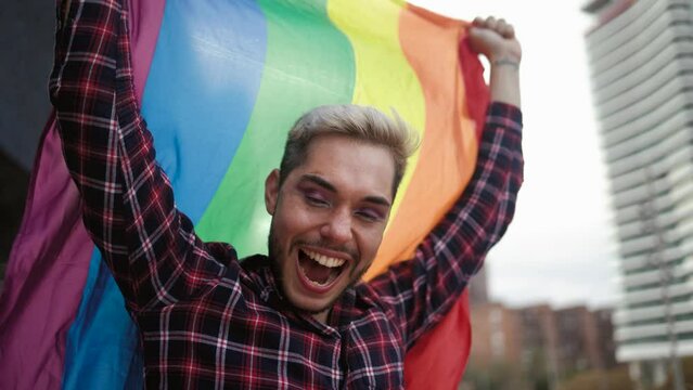 Happy gay man having fun holding rainbow flag symbol of LGBTQ community