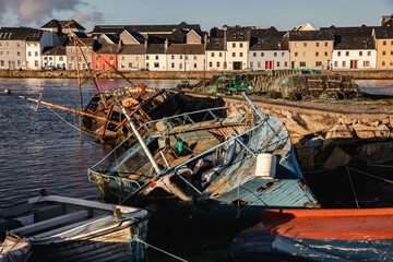 Fototapeta na wymiar Old wooden shipwrecks in Claddagh Bay, Galway, sunny day in beautiful and popular tourist spot with colourful houses in the background and waters of Atlantic Ocean - best Ireland