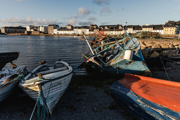 Old wooden shipwrecks in Claddagh Bay, Galway, sunny day in beautiful and popular tourist spot with colourful houses in the background and waters of Atlantic Ocean - best Ireland