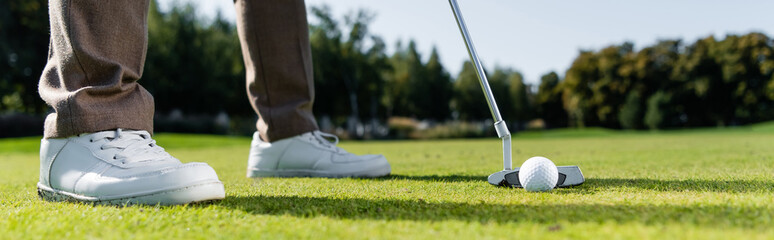 cropped view of man in white sneakers playing golf on lawn, banner.