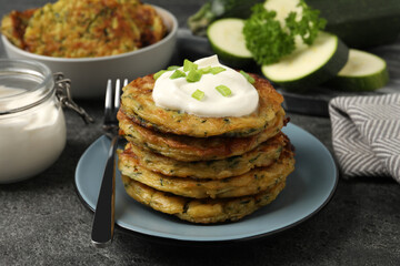 Delicious zucchini pancakes with sour cream and green onion served on grey table, closeup