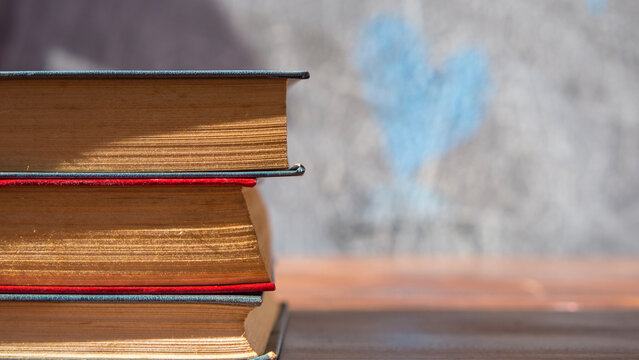 Banner: A stack of books on a dark gray blackboard background with painted hearts and a place to copy. The concept of education is books on the table in the classroom