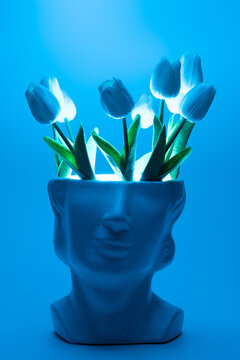Marble head flower pot with tulips and teal led background. Contrast artistic concept.