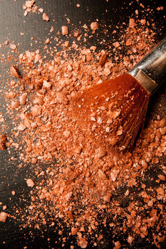 Brushes for makeup on a black background with beige powder. Brown face powder and makeup brushes on black background. The concept of beauty and cosmetics. Crumpled face powder and makeup brushes