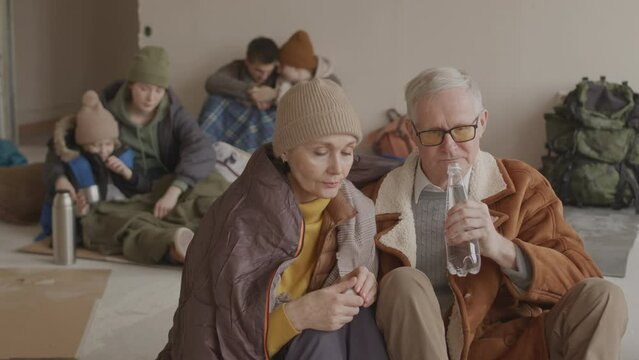 Slowmo of sad mature couple staying in cold asylum together with other refugees having conversation