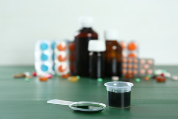 Dosing spoon and measuring cup with cough syrup on green wooden table. Space for text