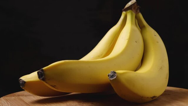 Close-up of ripe yellow bananas on a wooden surface spinning against a dark background. The camera flies around. Parallax effect