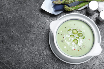 Bowl of delicious asparagus soup on grey table, flat lay. Space for text