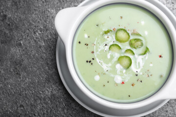 Bowl of delicious asparagus soup on grey table, top view. Space for text