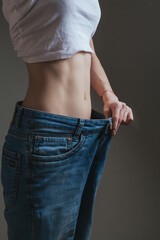 young woman dressed in wide jeans and a white shirt, demonstrates successful weight loss. concept...