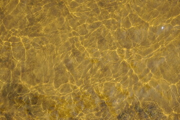 Fototapeta na wymiar Amber Colored Ripples of Water Over Clay as Background