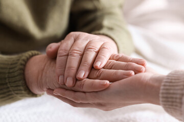 Young and elderly women holding hands together indoors, closeup
