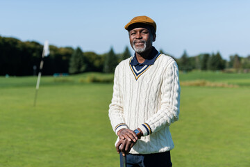 cheerful african american man standing with golf club on green field.