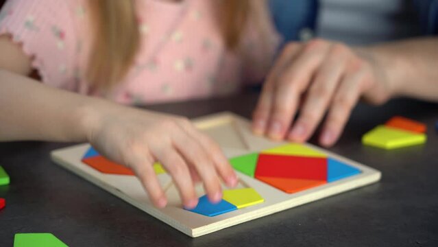 Childrens hands put colored tangram puzzle. Family spends leisure time collect wooden jigsaw. Education