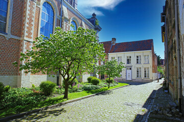 Lier (Begijnhof), Belgium - April 9. 2022: View on idyllic medieval cobblestone street, church garden, residential old homes, blue sky