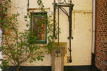View on front yard of medieval house with ancient water pump, tree, window - Lier (Begijnhof), Belgium